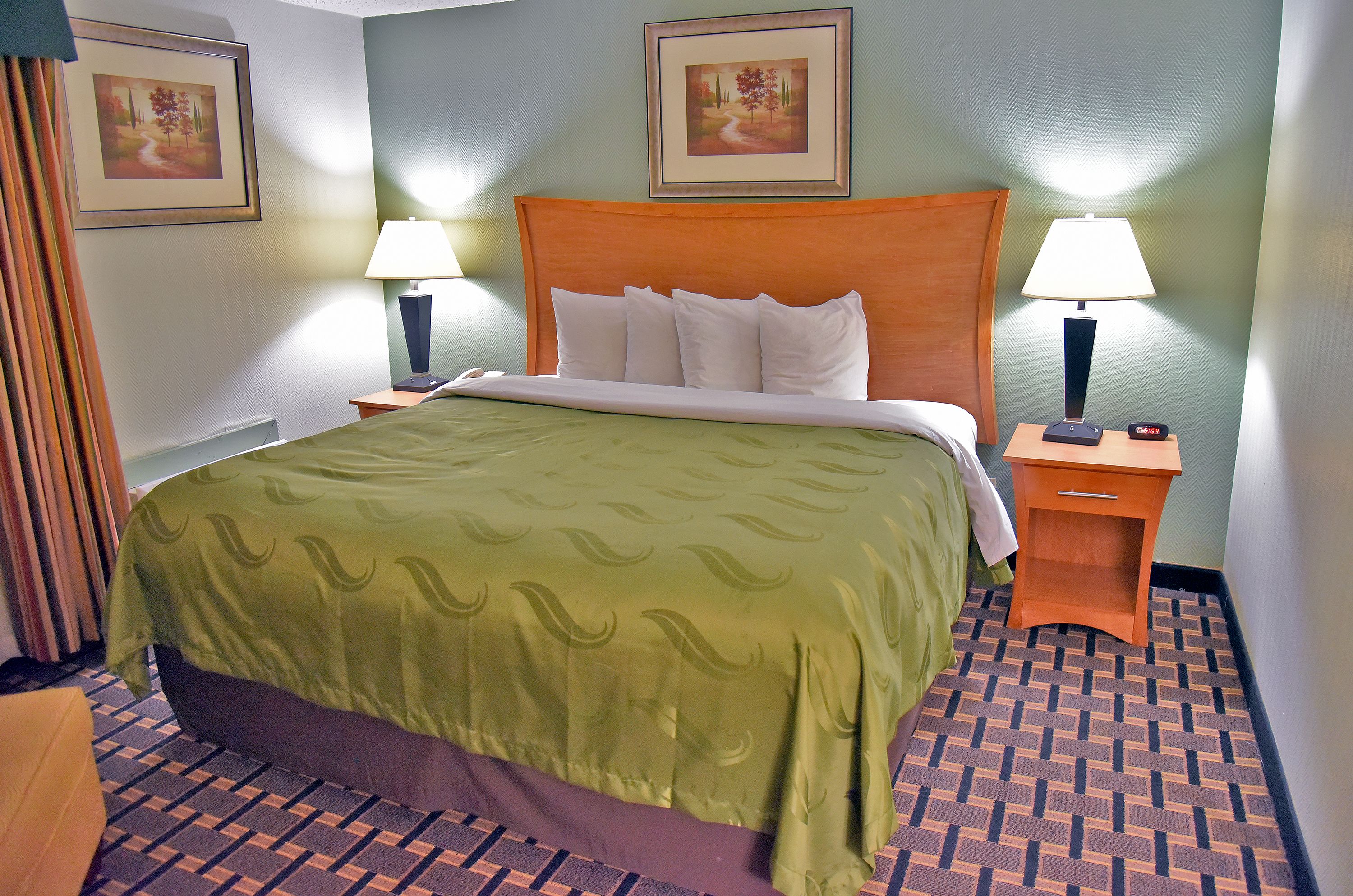 Una habitación de hotel con una cama grande, dos mesitas de noche con lámparas y dos cuadros enmarcados en las paredes.