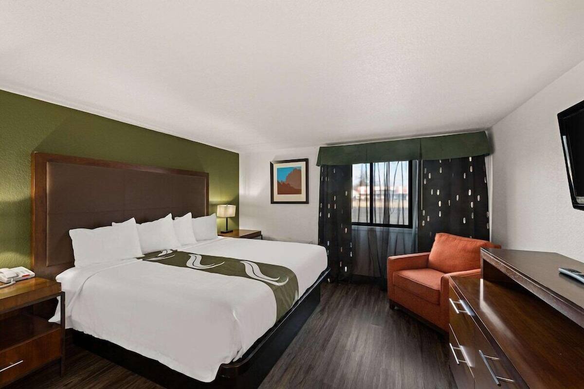 A hotel room with a bed, a desk, a chair, a TV, and a window with curtains.