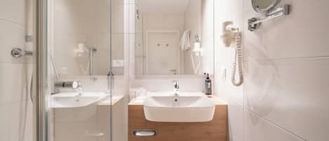 A modern bathroom with two sinks, a glass shower enclosure, and a hairdryer mounted on the wall.