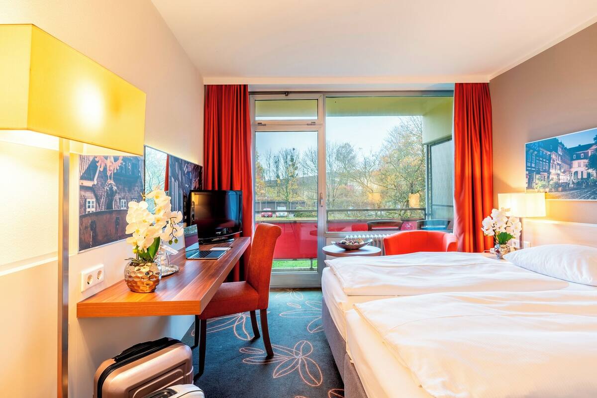 A hotel room with a bed, desk, chair, TV, and a view of the outdoors.