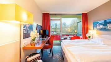 A hotel room with a bed, desk, chair, TV, and a view of the outdoors.