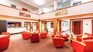 Un vestíbulo de hotel con asientos rojos, un mostrador de recepción y un techo alto con vigas de madera.