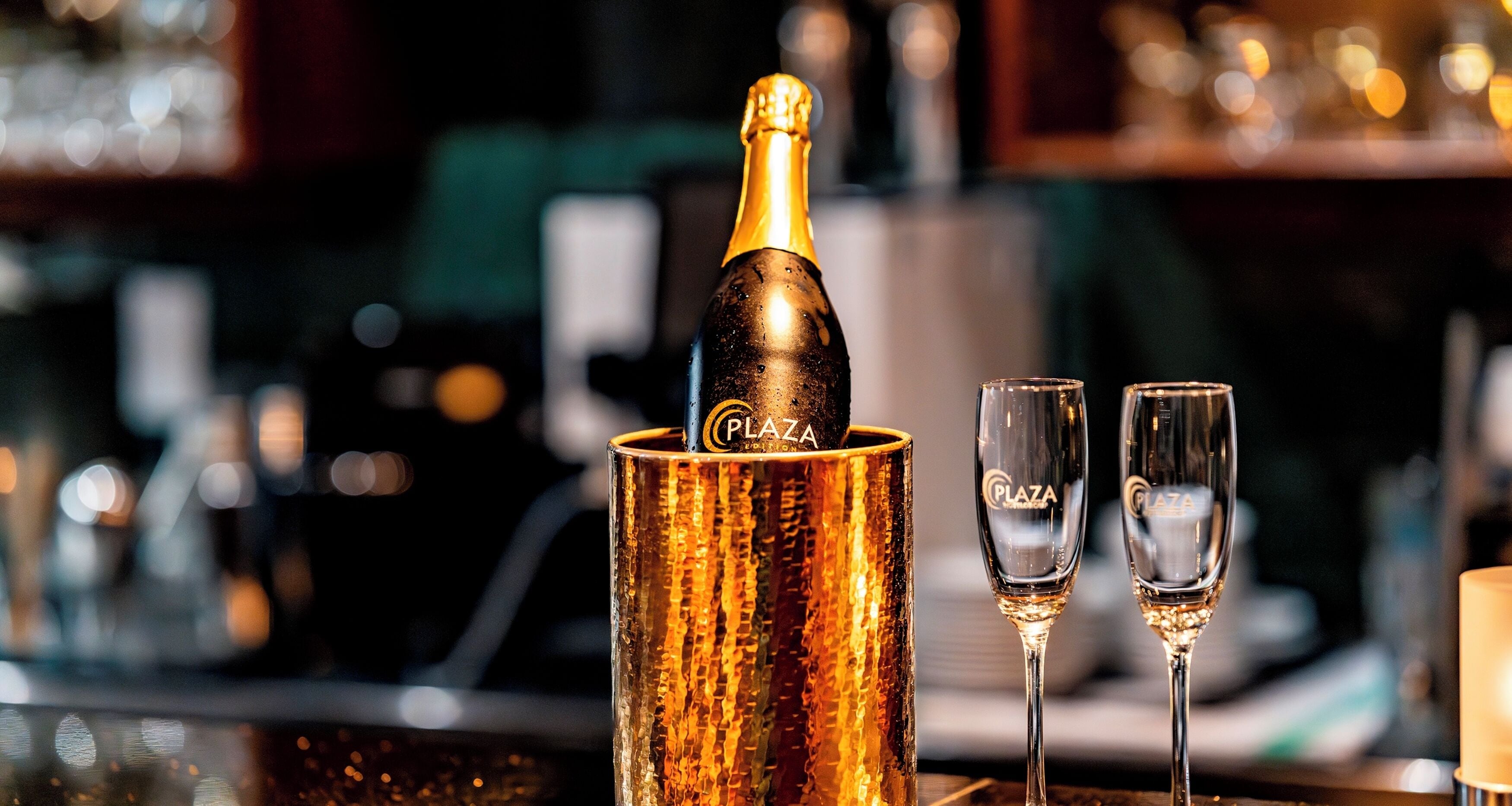Eine Champagnerflasche in einem goldenen Behälter mit zwei Gläsern daneben.