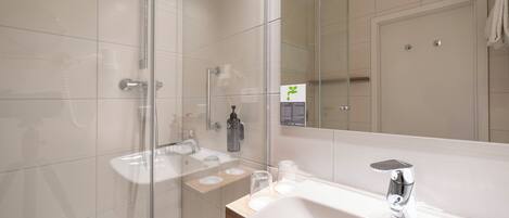 Une salle de bain moderne avec une douche à l’italienne en verre, un lavabo blanc et un grand miroir.