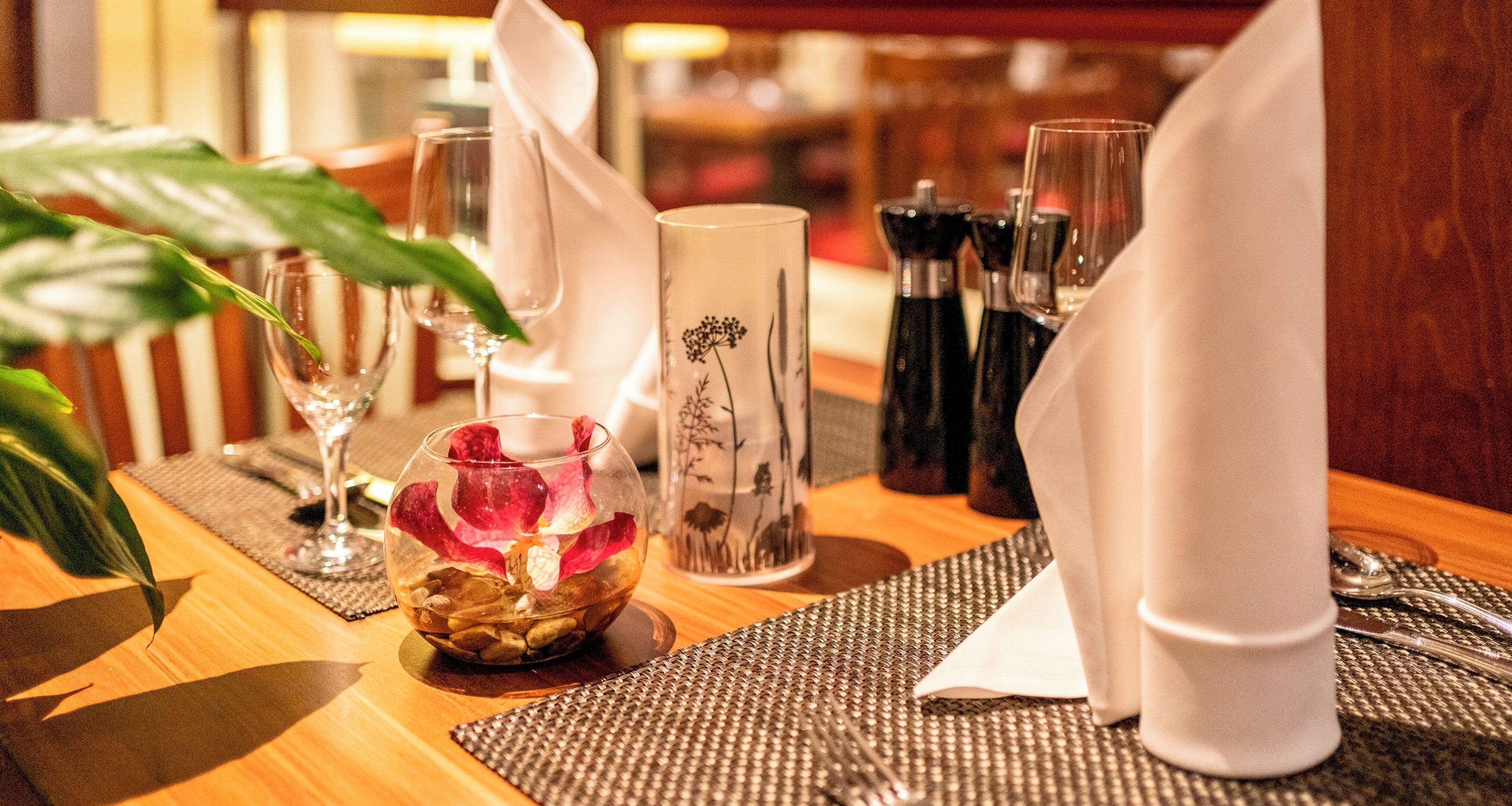 A dining table set with a clear glass bowl, a white vase with a floral design, and a white napkin.