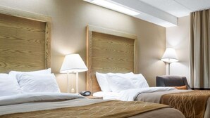 Habitación de hotel con dos camas, cabeceros de madera, lámparas de noche, una silla y una mesita de noche con teléfono.