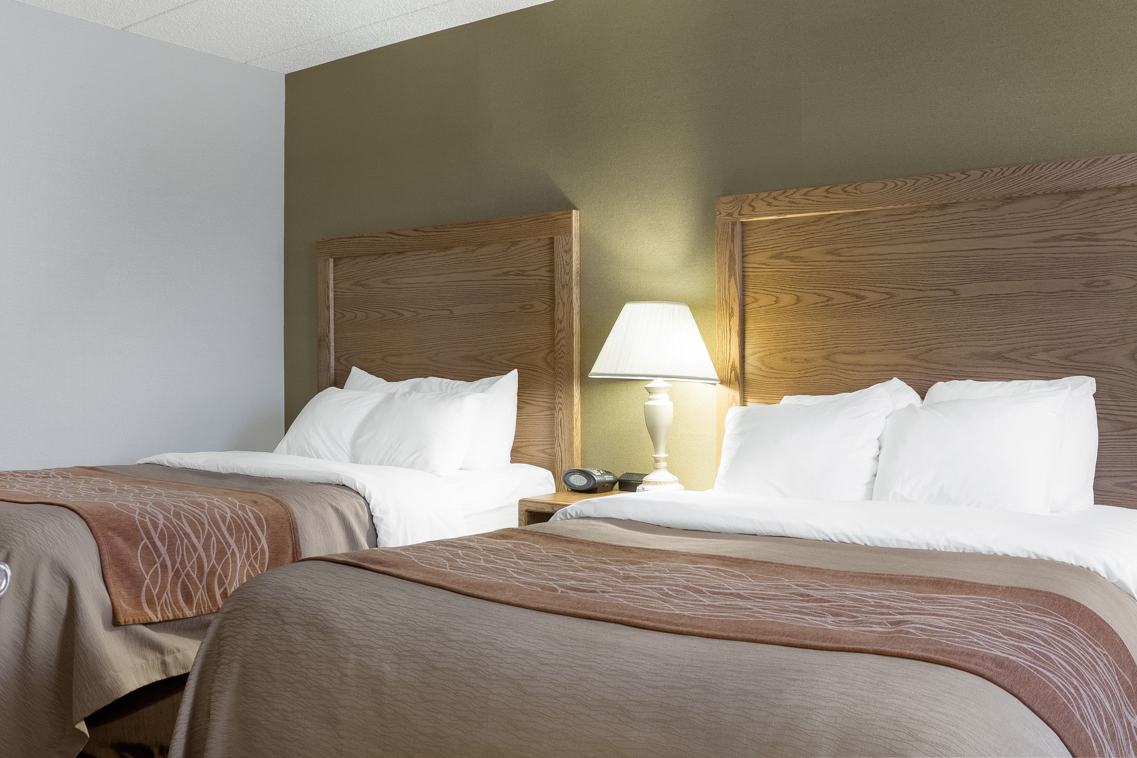Una habitación de hotel con dos camas, una mesita de noche con lámpara y un cabecero de madera.