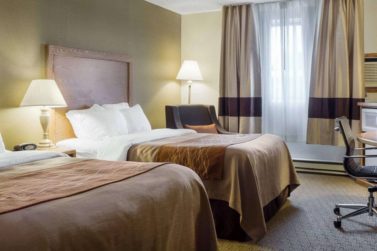 A hotel room with two beds, a desk, a chair, and a window with curtains.