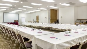 Un salón de conferencias con largas mesas, sillas y equipo de presentación.