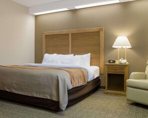 A hotel room with a bed, a bedside table with a lamp, a chair, and a carpeted floor. - Quality Inn Bismarck I-94 (Bismarck)
