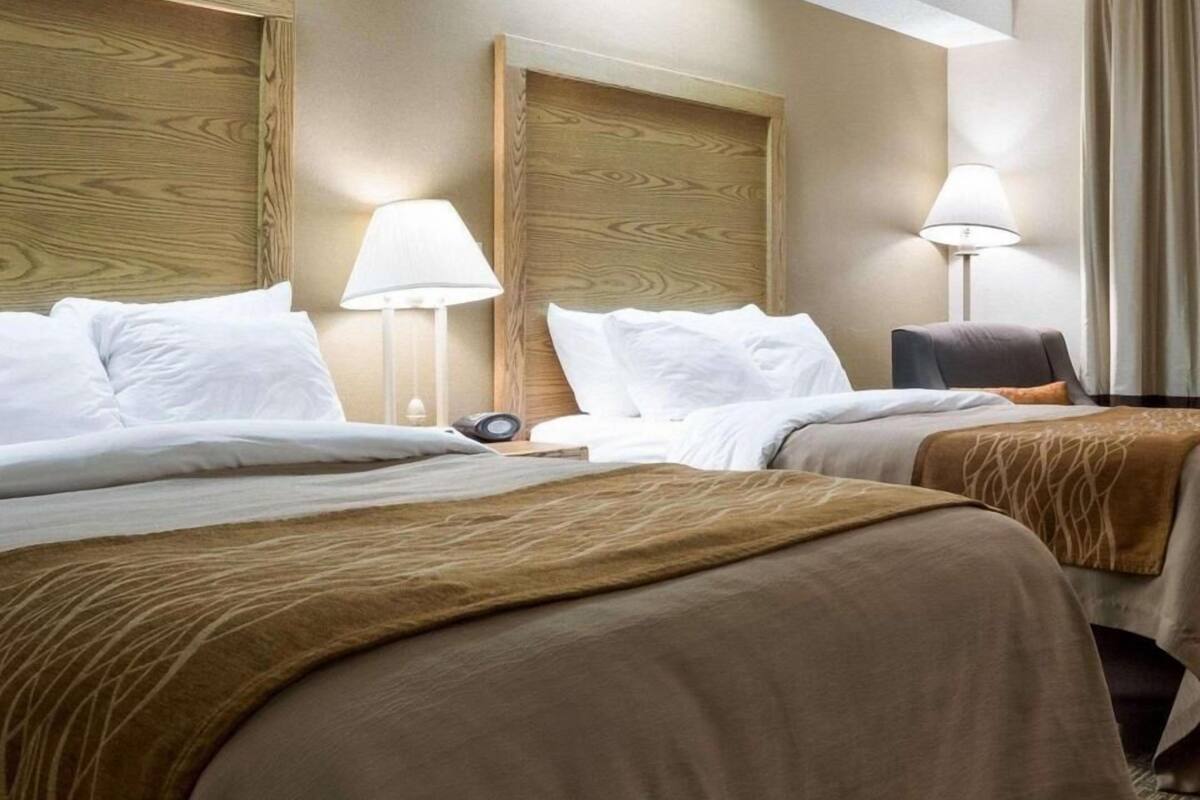 A hotel room with two beds, a desk, and two lamps.