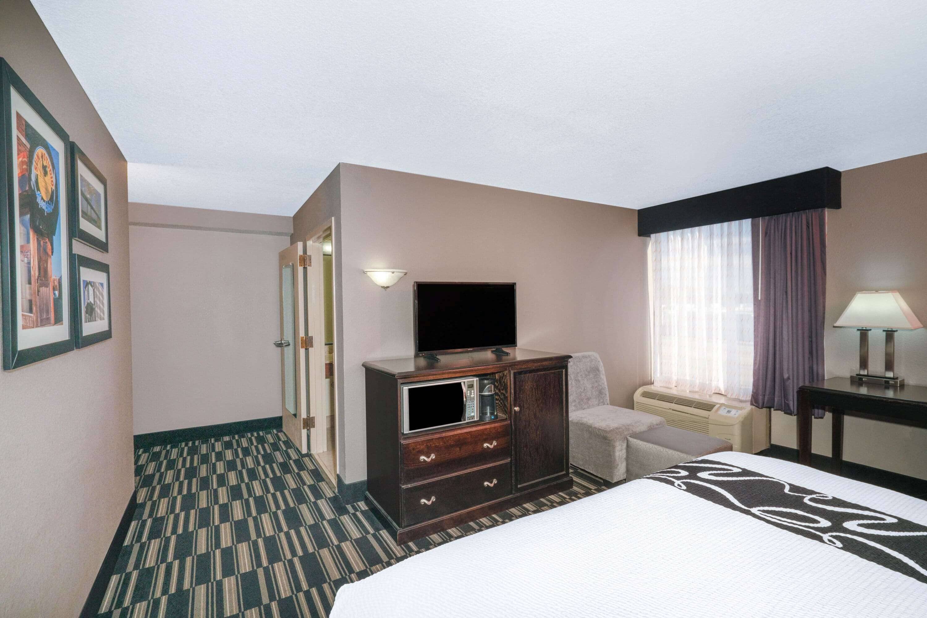 A hotel room with a bed, a dresser, a television, a chair, a desk, and a window with curtains.
