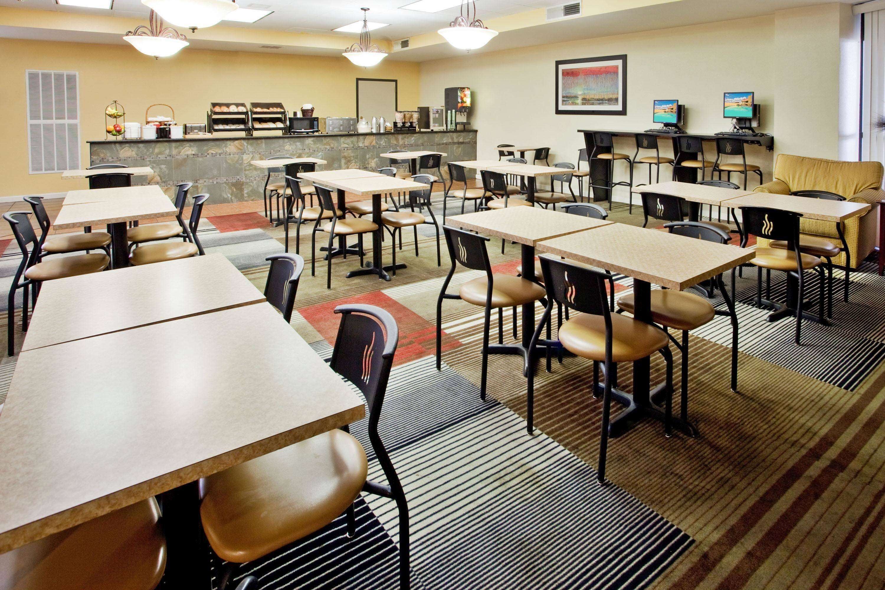 A hotel dining area with multiple tables and chairs, a counter with baked goods, and a television screen.