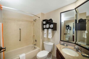 A bathroom with a bathtub, toilet, and sink. There are shelves with towels and toiletries.