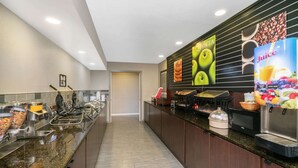 A hotel breakfast area with a long counter, various food stations, and a juice dispenser. - La Quinta Inn & Suites by Wyndham Memphis Airport Graceland (Memphis)