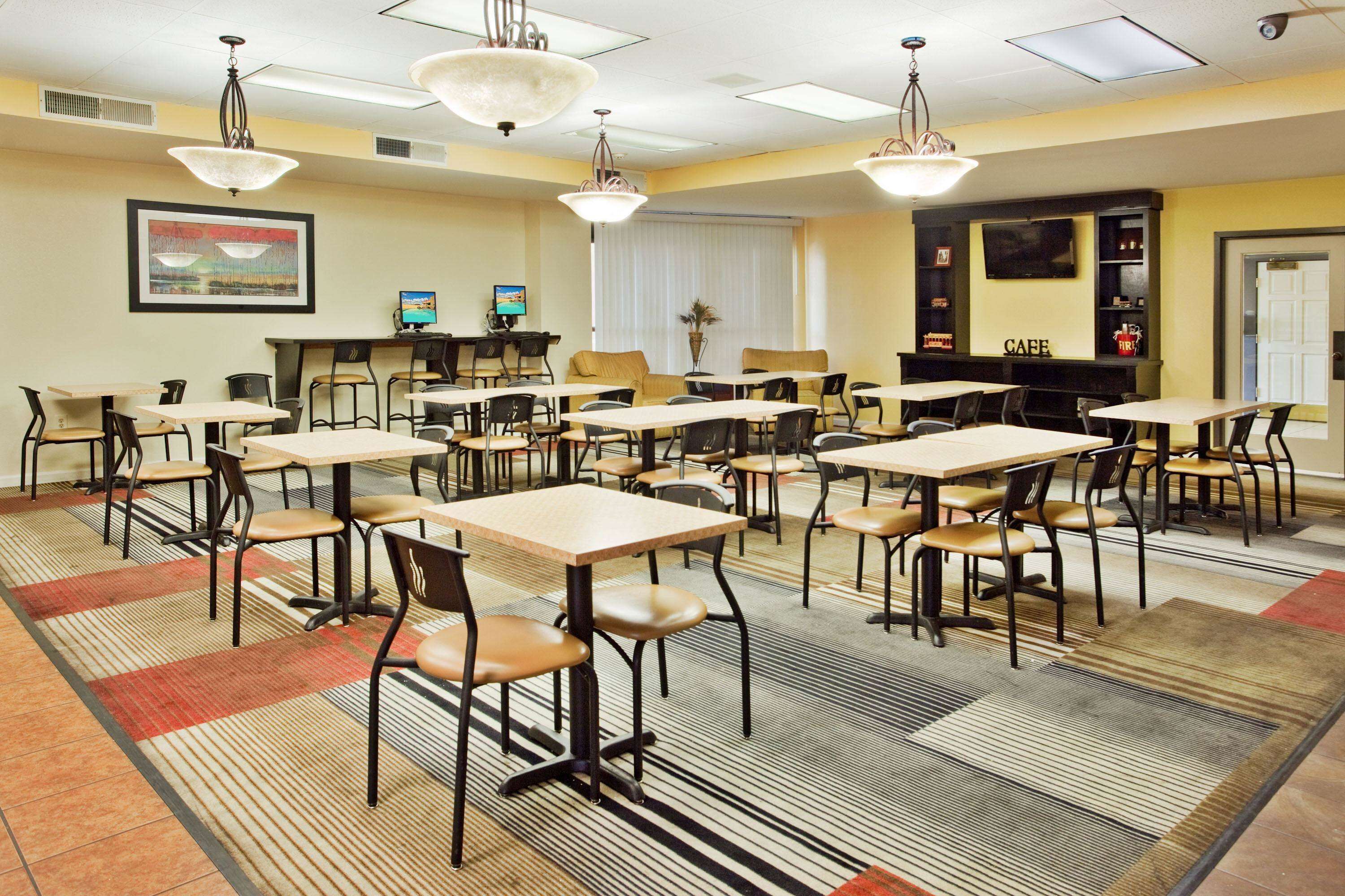 Uma sala de jantar de hotel com várias mesas e cadeiras, uma lareira e uma televisão na parede.