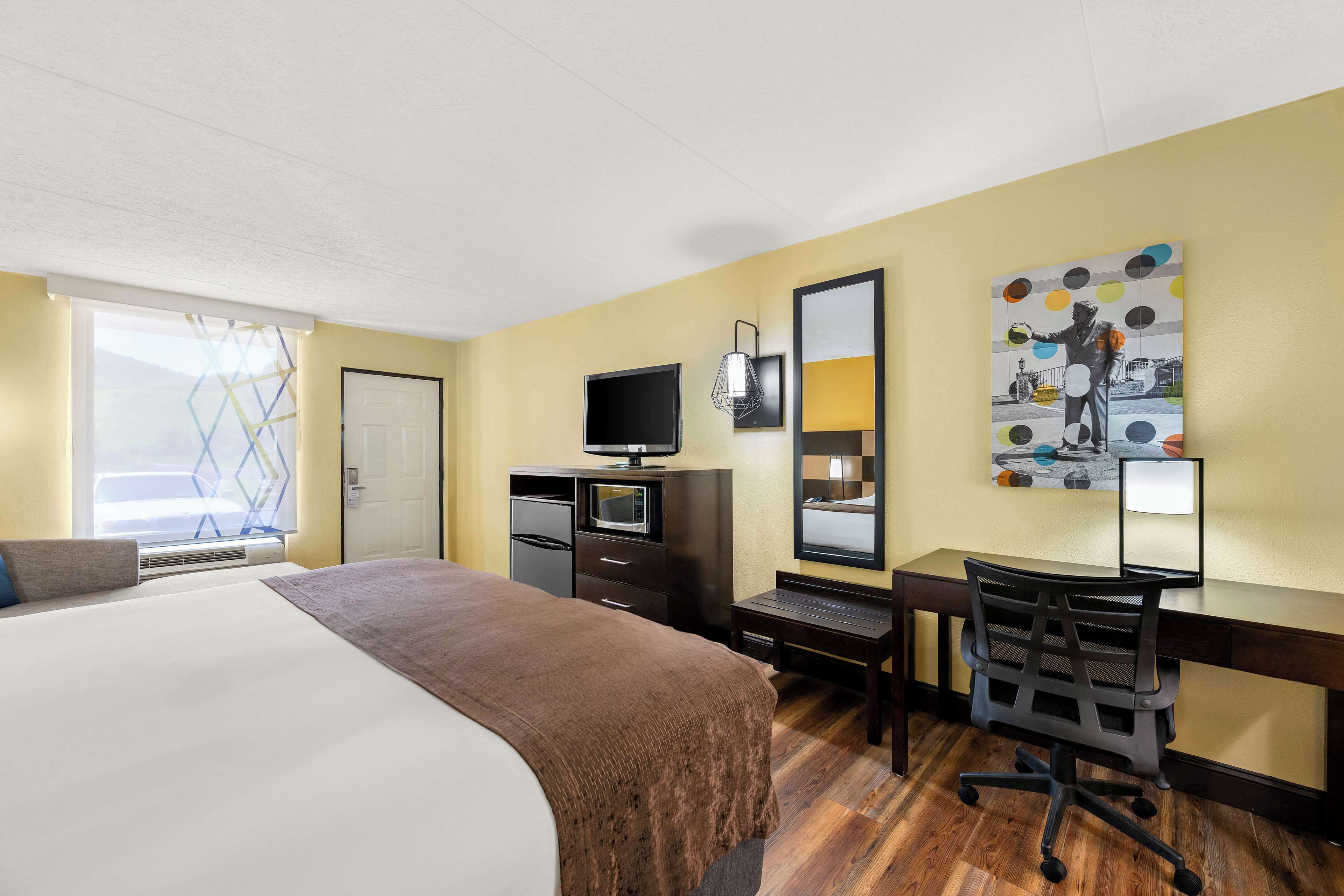 A hotel room with a bed, desk, chair, television, and artwork on the wall.