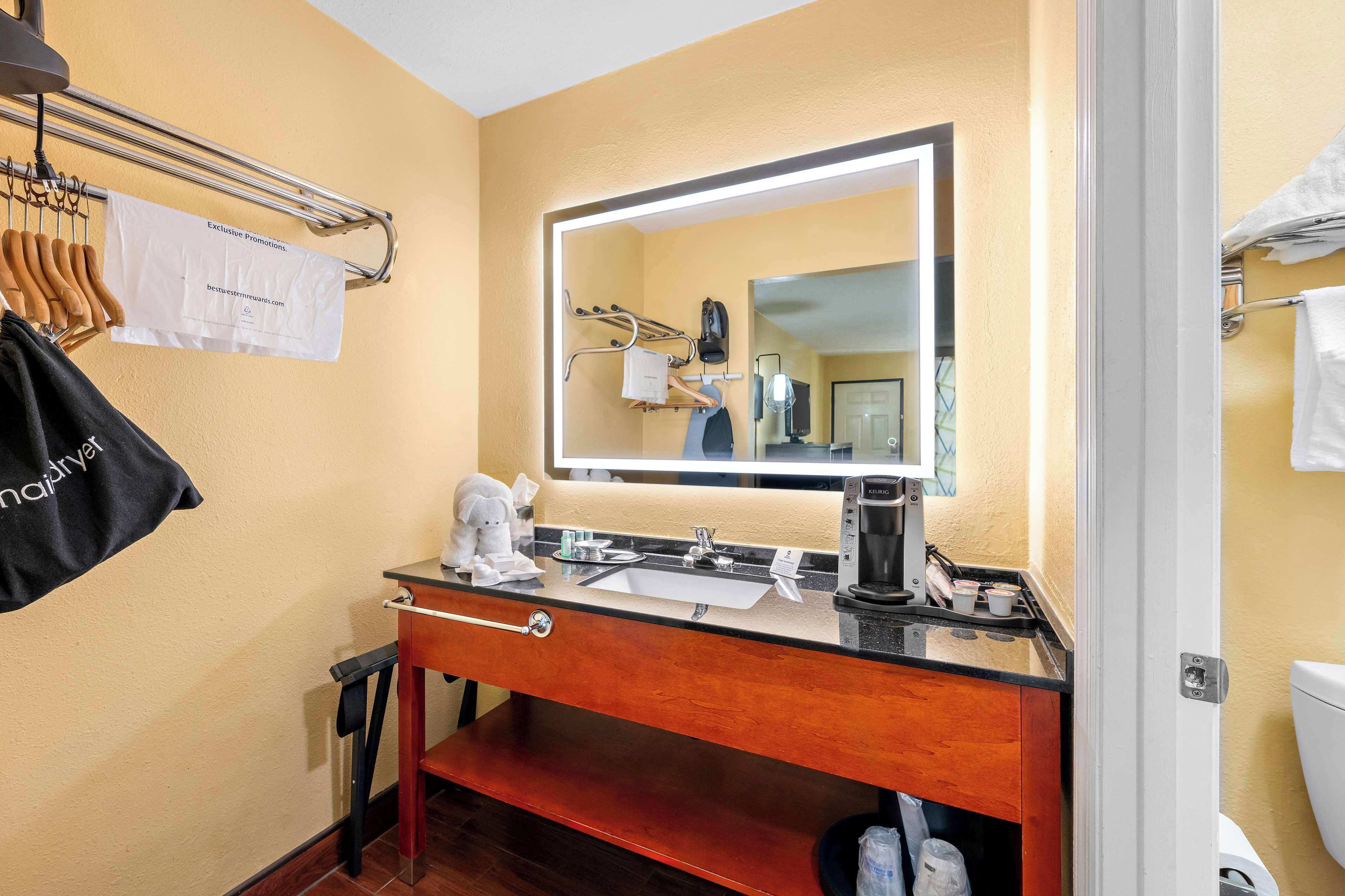 A hotel bathroom with a sink, mirror, towel rack, and a coffee maker.