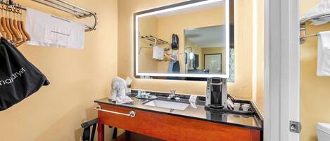 Een hotelbadkamer met een wastafel, spiegel, handdoekhouder en een koffiezetapparaat.