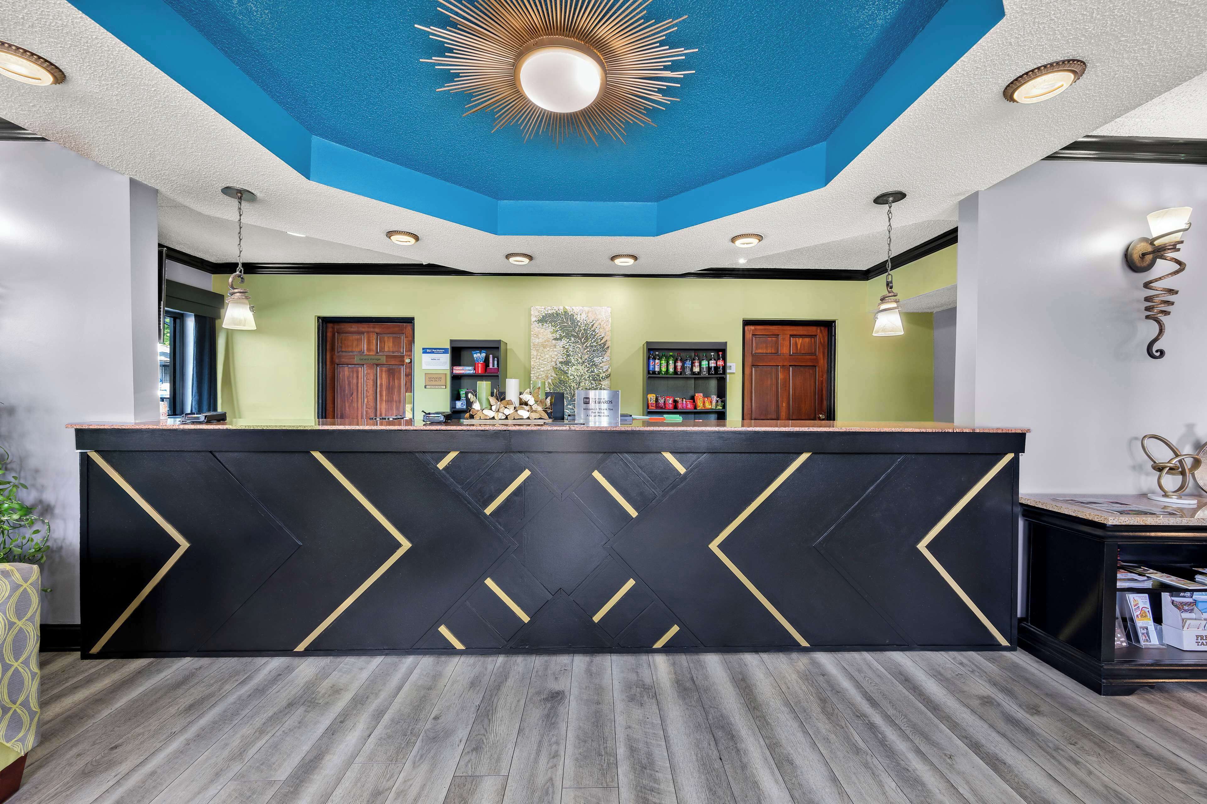 Un espace d’accueil doté d’un comptoir noir orné de chevrons dorés, d’un plafond bleu avec un luminaire en forme de soleil et de meubles en bois.
