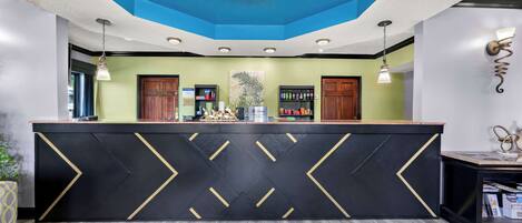 Un espace d’accueil doté d’un comptoir noir orné de chevrons dorés, d’un plafond bleu avec un luminaire en forme de soleil et de meubles en bois.