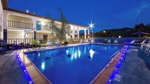 A swimming pool with a wooden deck, lounge chairs, and a building with arched windows and a balcony.
