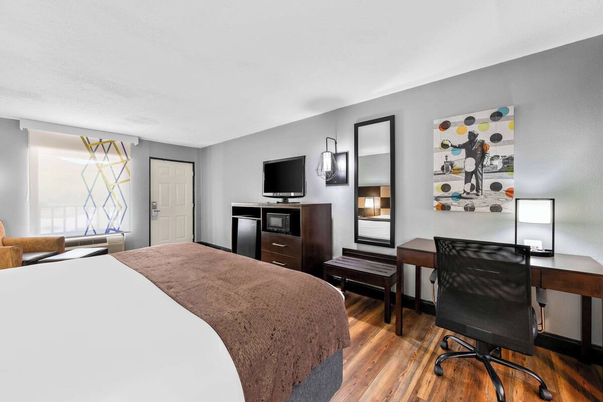 A hotel room with a bed, a desk, a chair, a TV, and a mirror.