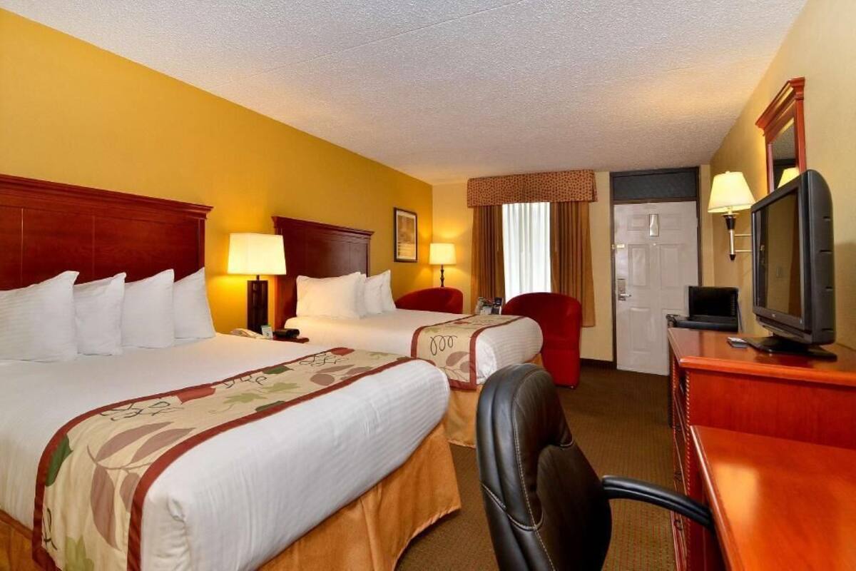 A hotel room with two beds, a desk with a television, and a door.
