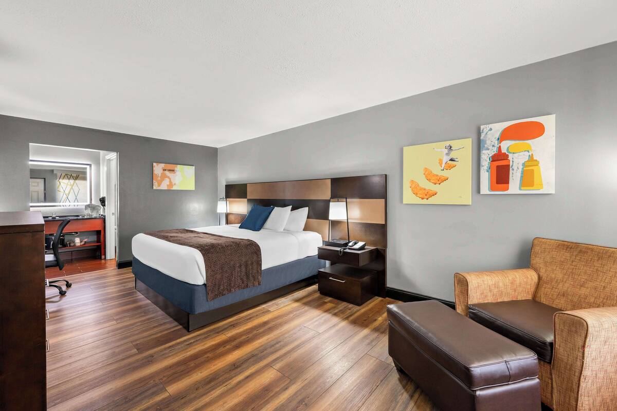 A modern hotel room with a large bed, a desk, a chair, and artwork on the walls.