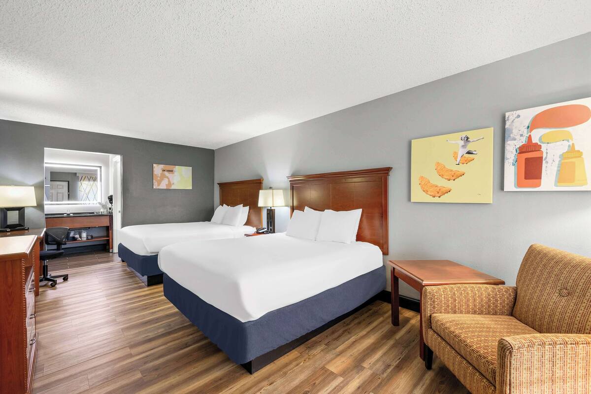 A hotel room with two beds, a desk, a chair, and artwork on the walls.