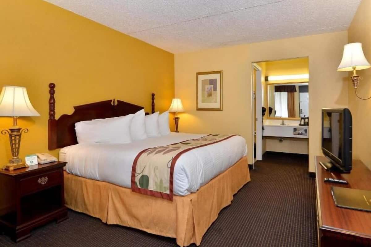 A hotel room with a bed, bedside lamps, a nightstand, a desk with a computer, and a mirror.