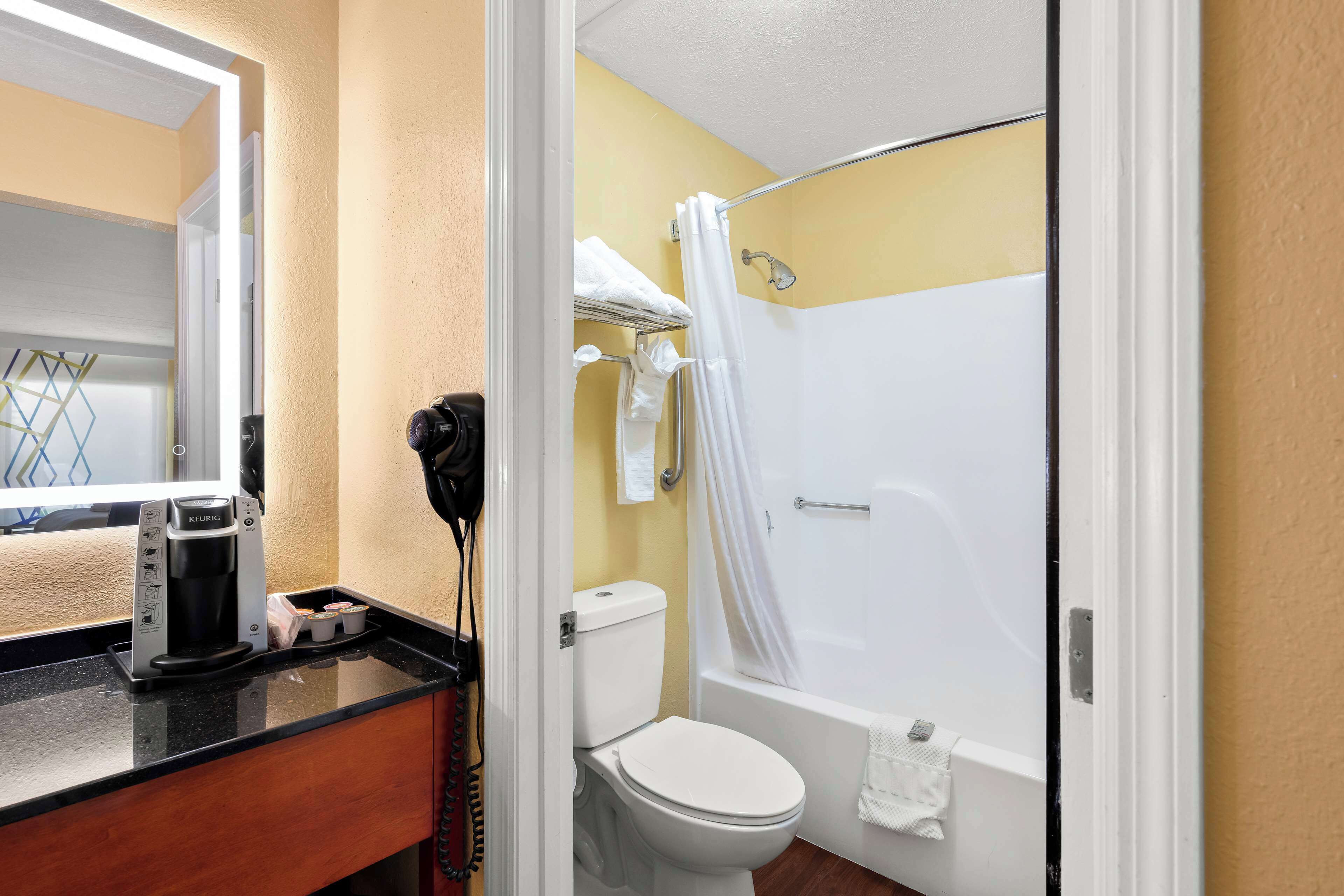 Une salle de bain équipée de toilettes, d’une douche avec un rideau, d’un porte-serviettes et d’une machine à café posée sur le comptoir.