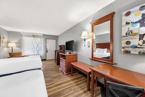 A hotel room with a bed, a desk, a chair, a television, a dresser, and a mirror.