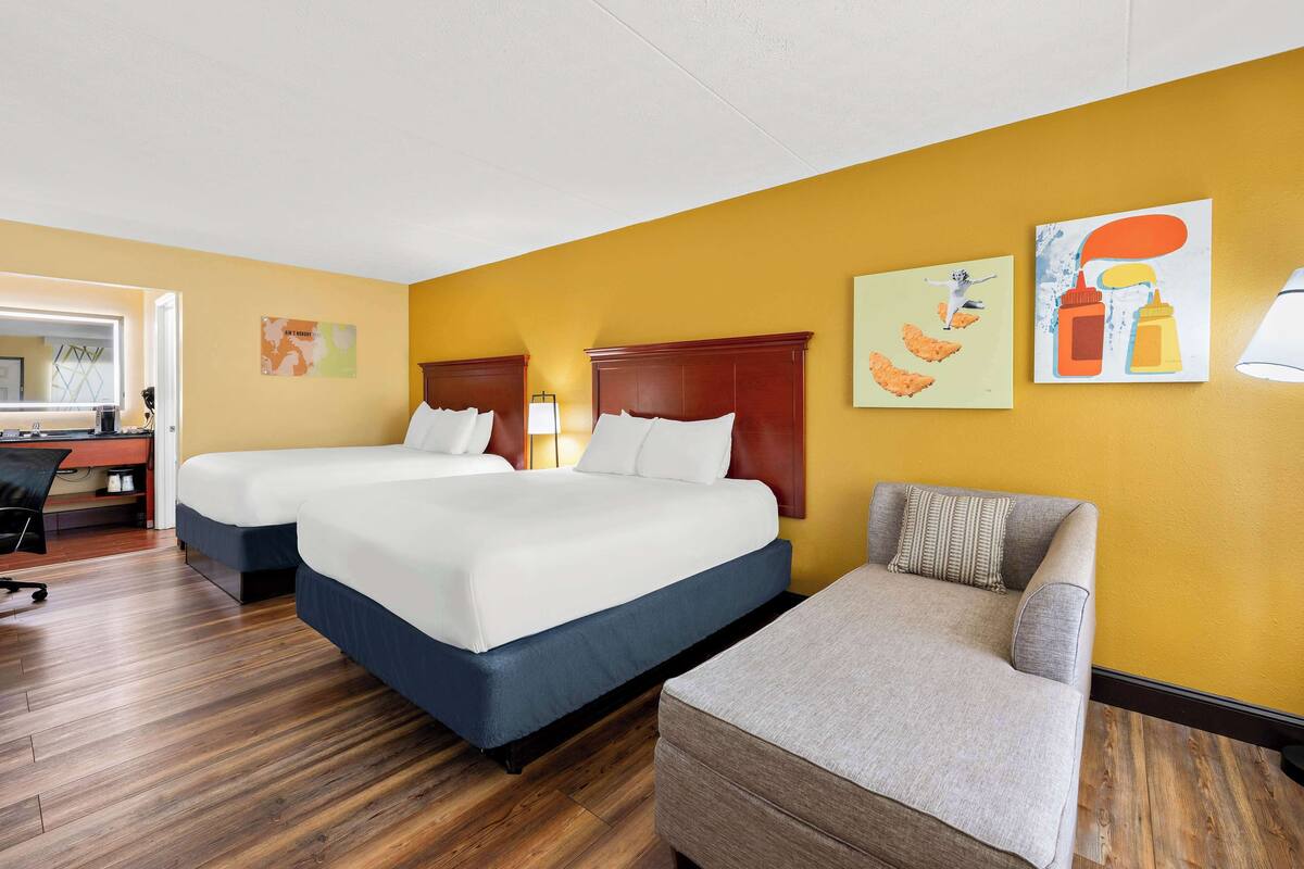 A hotel room with two beds, a desk, and a chair.