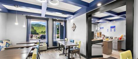 A modern dining area with a view of the outdoors, a kitchen area, and a seating arrangement with tables and chairs.