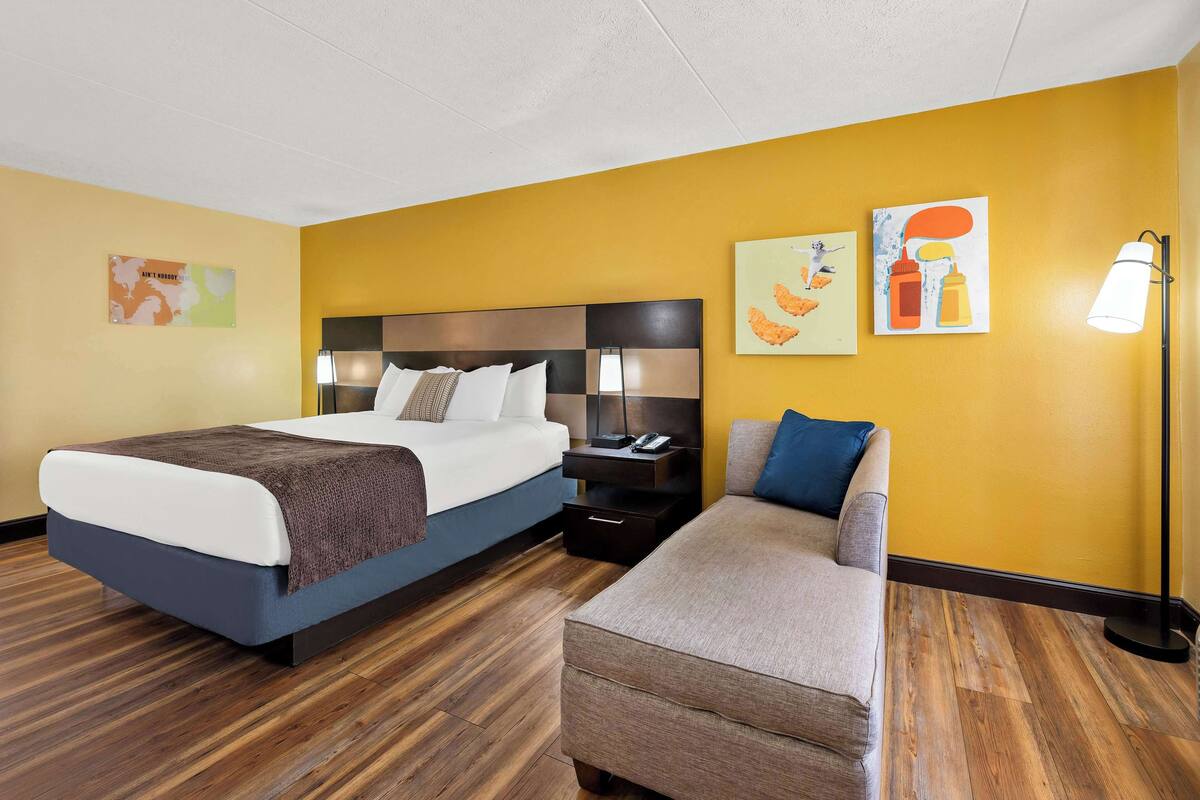 A hotel room with a bed, a sofa, a nightstand, and artwork on the walls.