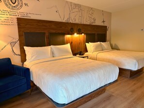A hotel room with two beds, a wooden headboard, a blue armchair, and a wall map.