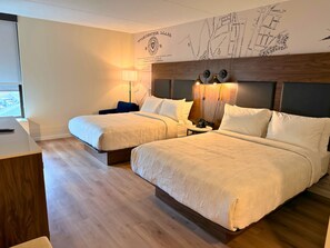 Una camera d'albergo con due letti, una scrivania, una lampada e una mappa appesa al muro.