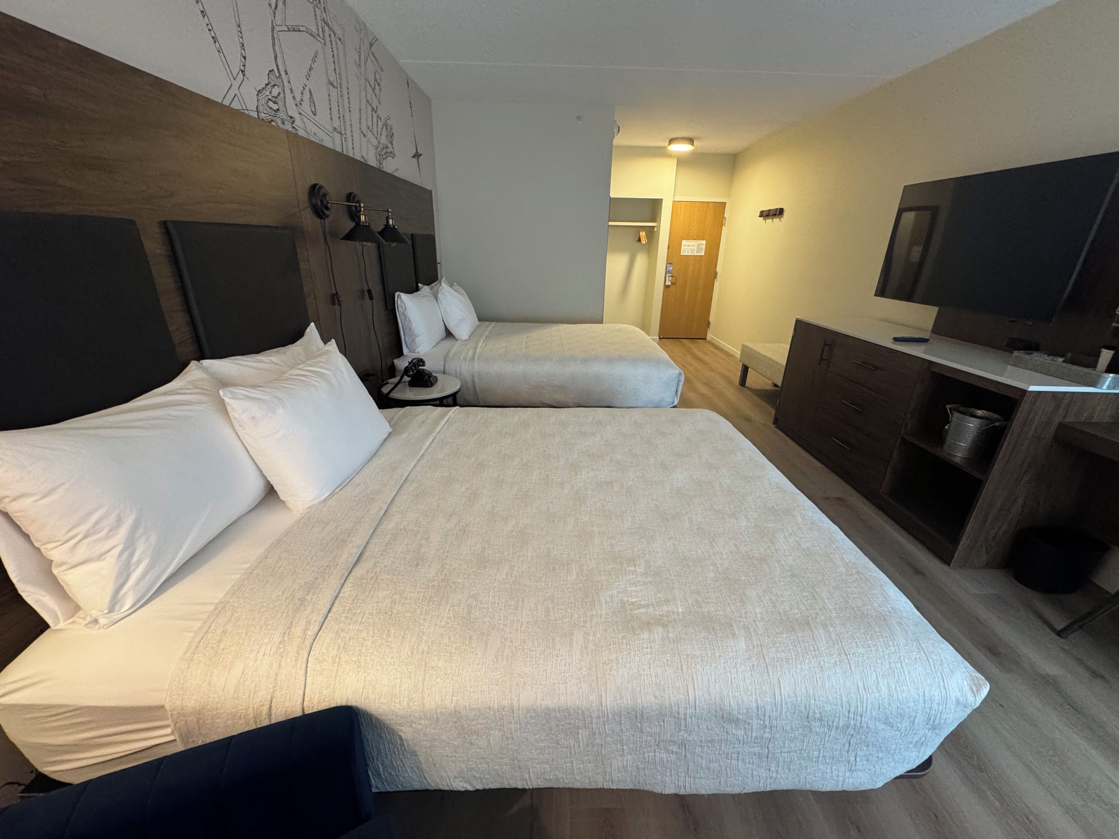 A hotel room with two beds, a desk, a television, and a wall with a map.