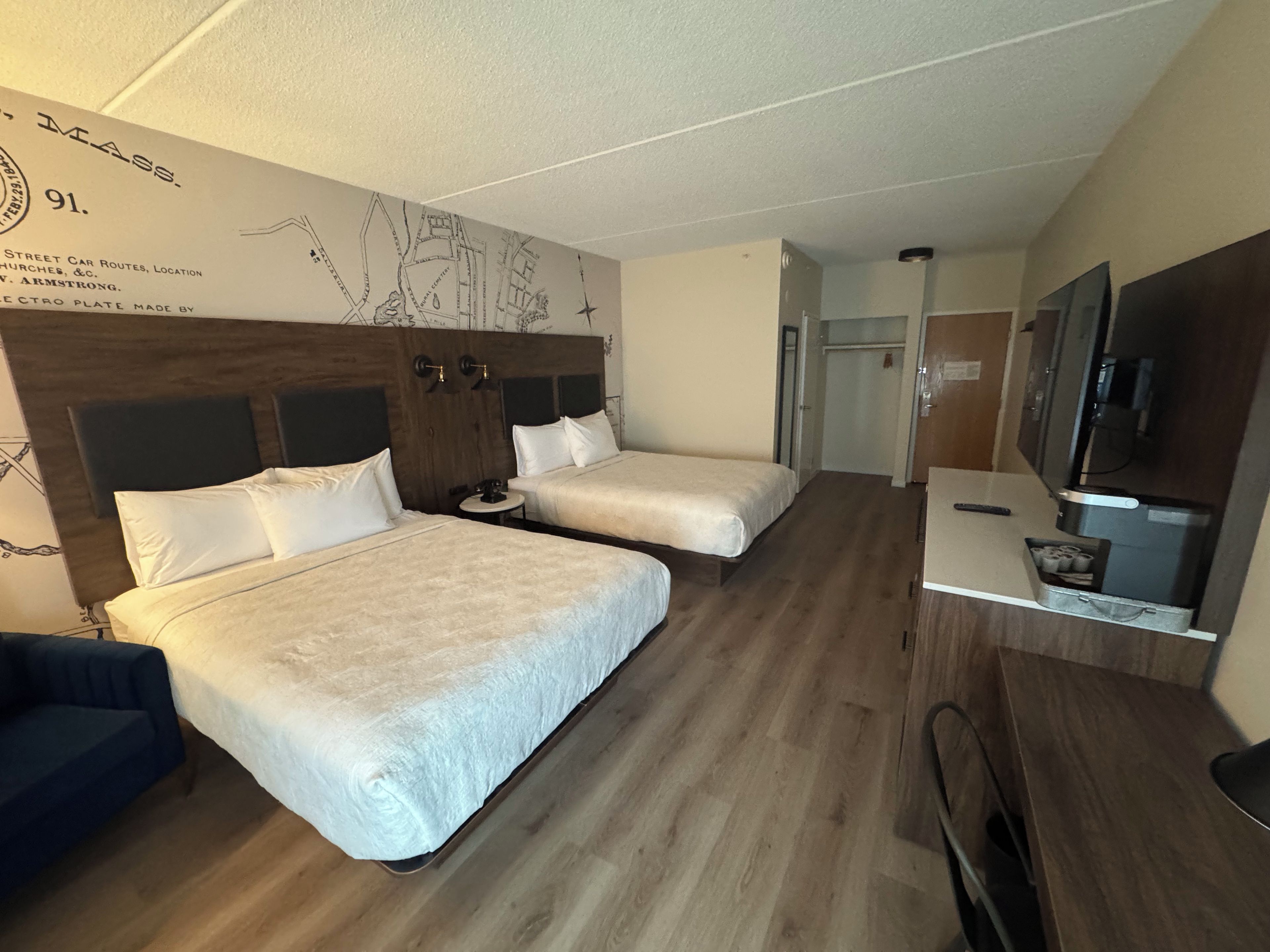 A hotel room with two beds, a small round table, a TV, and a wardrobe.