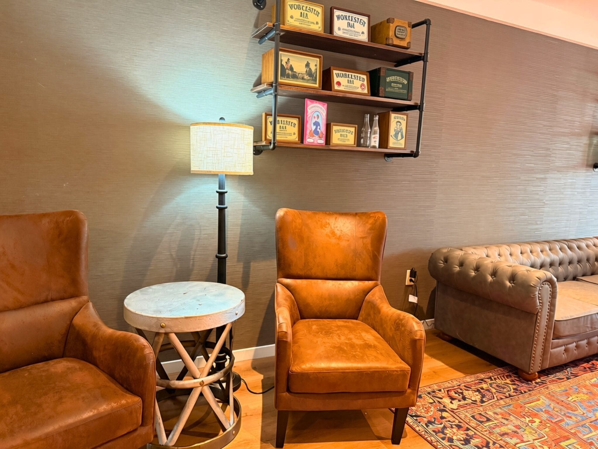 A room with a brown leather armchair, a round table, a tufted sofa, and a shelf with vintage items.