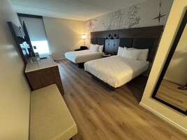 Habitación de hotel con dos camas, un escritorio, un banco y un mapa mural.
