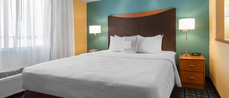 Una habitación de hotel con una cama grande, dos lámparas de noche, una mesita de noche de madera y una ventana con cortinas translúcidas.
