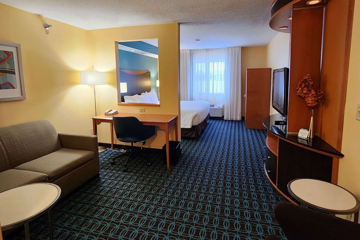 A hotel room with a bed, a desk, a chair, a small table, a TV, and a mirror.