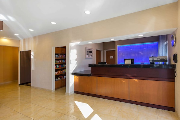 A hotel reception area with a wooden reception desk, a blue-lit wall, and a clock on the wall.
