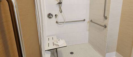 A bathroom with white tiled walls, a wooden door, a sink with a towel, and grab bars.