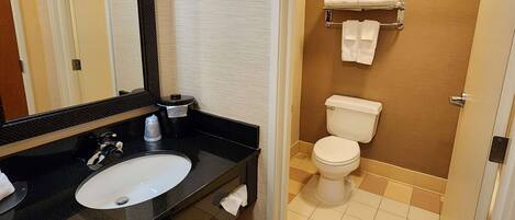 A bathroom with a black countertop sink, a mirror, a toilet, and a towel rack with towels.