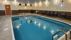 Une piscine intérieure avec un bord carrelé, un panneau indiquant qu’il est interdit de plonger, et un espace détente avec des chaises.