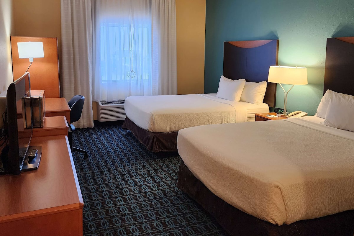 A hotel room with two beds, a desk with a computer, a telephone, and a lamp.