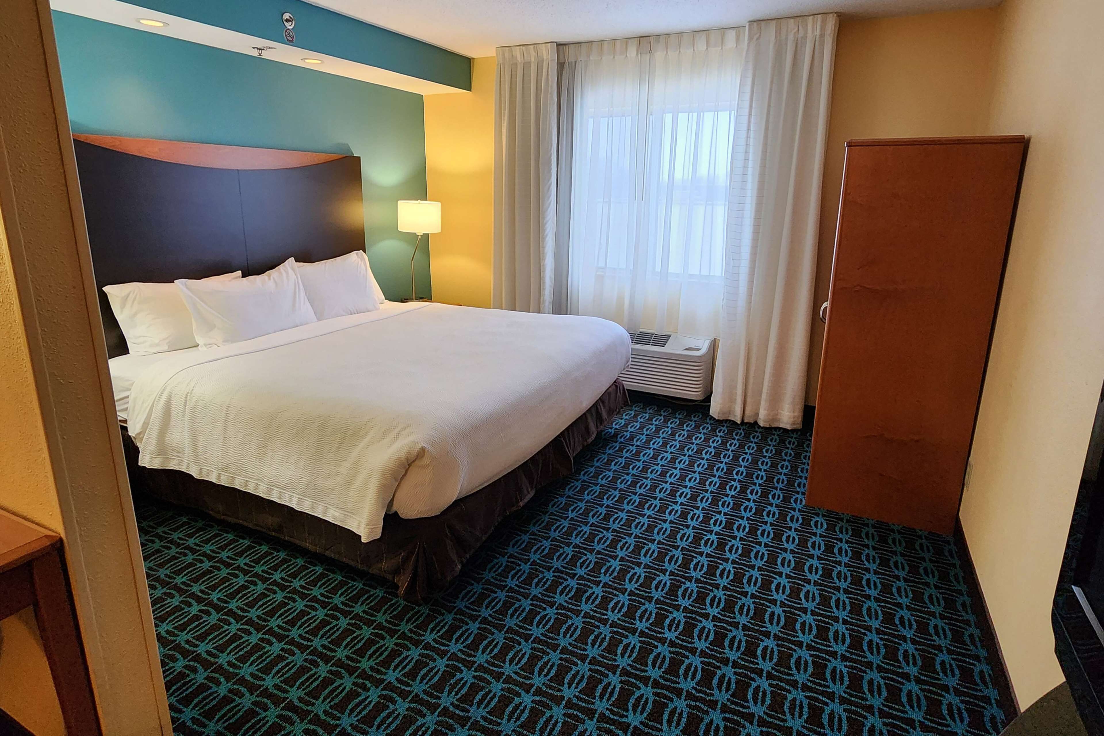 A hotel room with a bed, a desk, a lamp, a window with curtains, and a wardrobe.